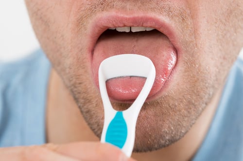 Periuta pentru curatarea limbii - foto blog oralix - close-up of mid adult man cleaning his tongue with scraper